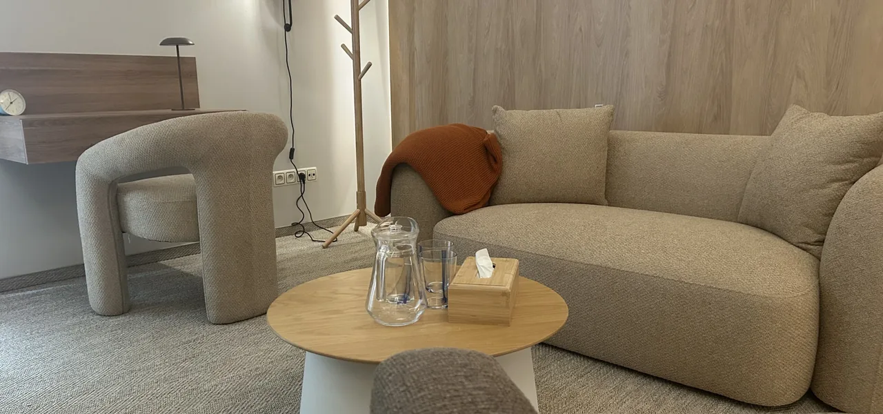 Gabinet VITA 72 — beżowa sofa, fotel i wieszak przy ścianie z drewna